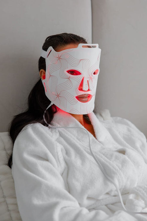 Person wearing a white facial mask with red lights, wrapped in a white robe.